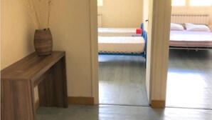A room with a wooden bench, a vase with dried flowers, and a bed with a blue chair.