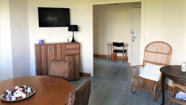 A dining area with a table set for two, a television mounted on the wall, and a ceiling fan.
