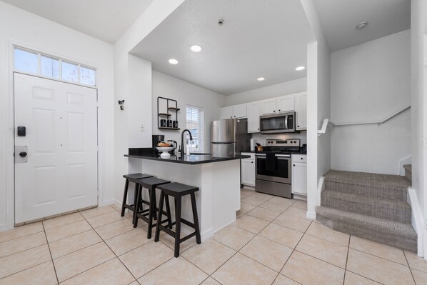 Kitchen features a central island with a refrigerator, microwave, and oven, along with white cabinetry and a black countertop.