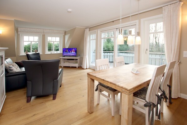 A spacious living room with a wooden dining table, two chairs, a sofa, and a television.