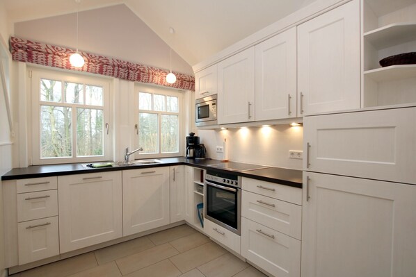 A modern kitchen with white cabinets, a black countertop, a built-in oven, and a microwave. - Comfort vacation apartment in Wyk, 4 persons, upper floor in 2-family house, 3 rooms, approx. 65m² (Wyk auf Föhr)