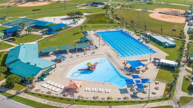 Vista aérea de un complejo deportivo con una gran piscina, varias canchas deportivas y un campo de béisbol.