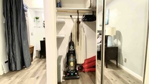 Una stanza con una porta scorrevole che dà su un armadio, un aspirapolvere e un piccolo tavolo con una lampada.