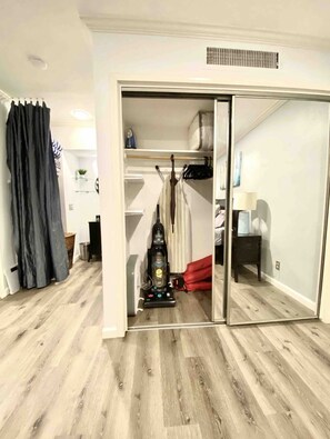 A room with a sliding door leading to a closet, a vacuum cleaner, and a small table with a lamp.