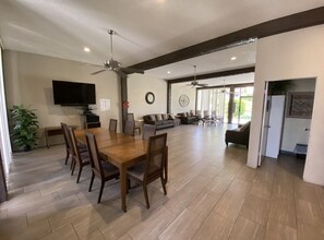 A spacious living area with a wooden dining table, sofas, and a TV mounted on the wall.