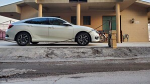 Un coche blanco aparcado frente a un edificio de fachada color beige y puerta verde.