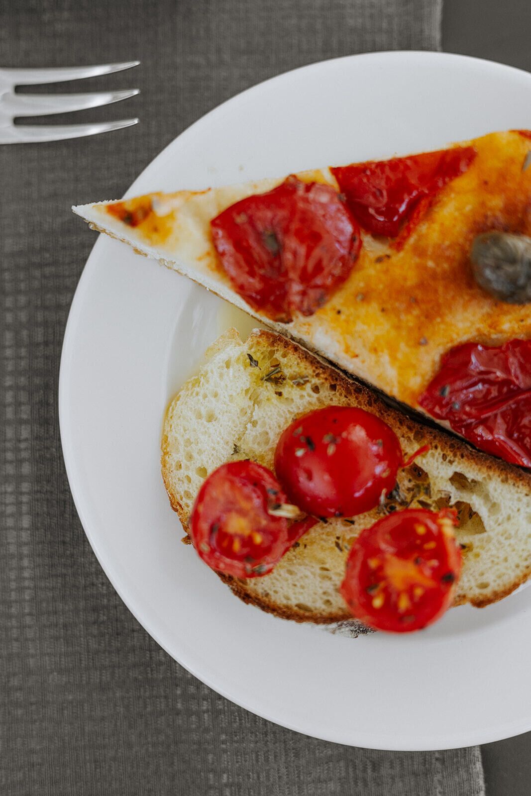 En bit pizza med tomatskivor på en vit tallrik.