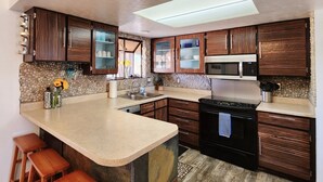 A kitchen with a central island, wooden cabinets, a microwave, and a stone backsplash. - Cozy Swell House- Pet Friendly, Fenced Backyard: 2 King Beds (Page)