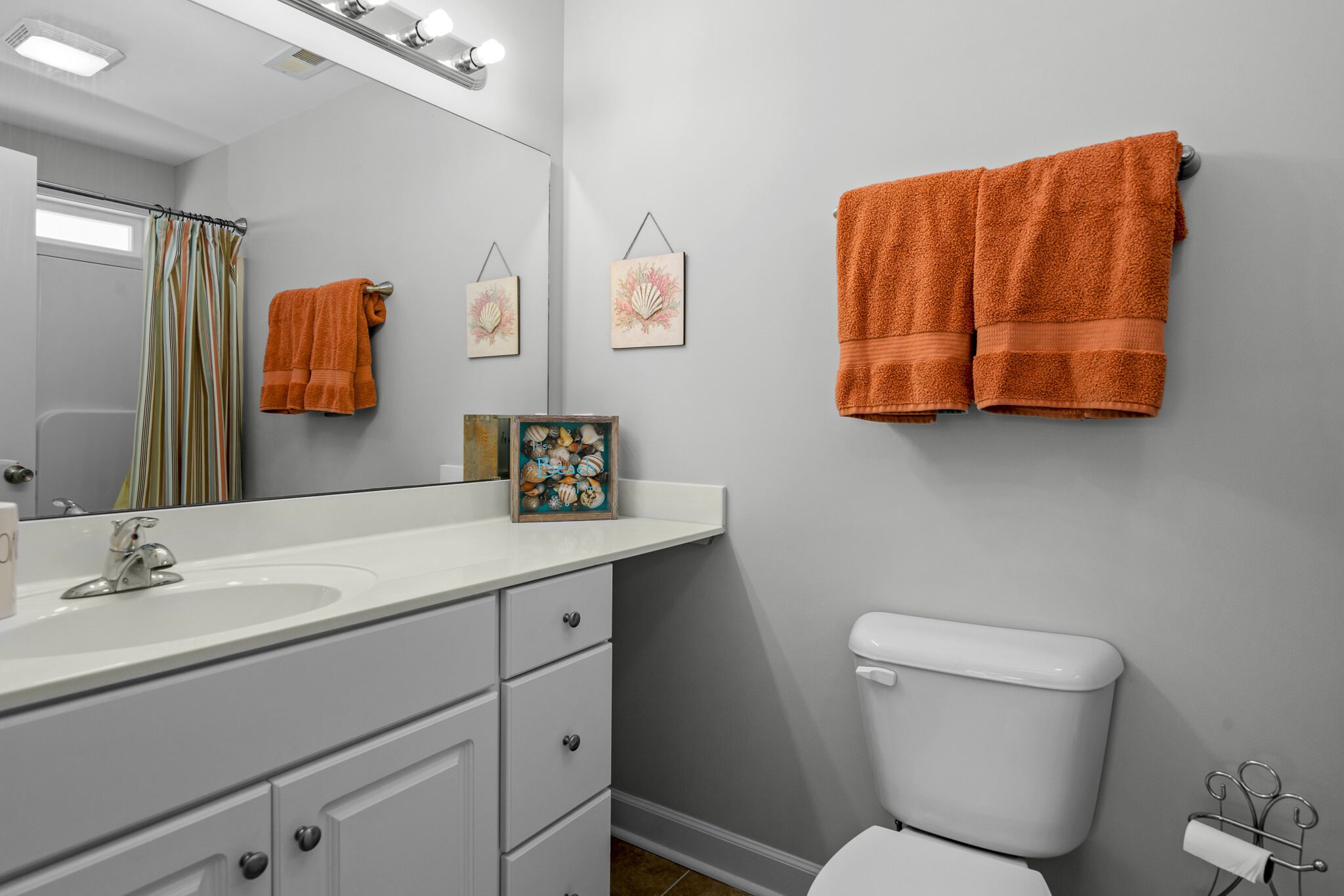 A bathroom with a white sink, a toilet, and two orange towels hanging on the wall.