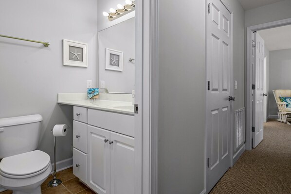 A bathroom with a toilet, sink, and cabinets. There are starfish decorations on the wall and a towel rack. - OCEANVIEW, 3 MIN WALK TO BEACH, KID-FRIENDLY, LINENS INCLUDED, FULLY STOCKED (Sunset Beach)