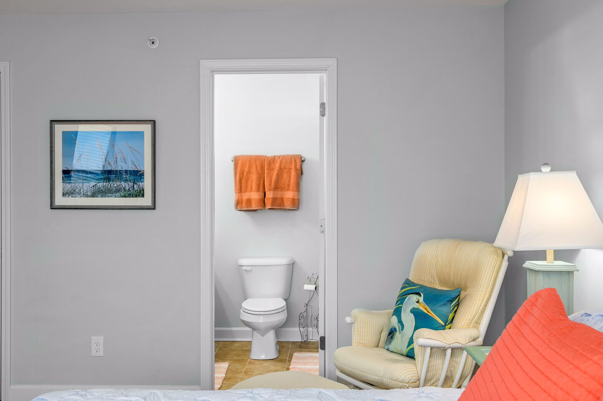 Une chambre à coucher avec un lit, une chaise, une lampe, des toilettes et un tableau encadré au mur.
