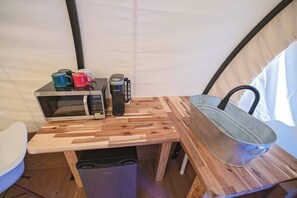 A compact kitchen with a microwave, coffee maker, and a metal pot on a wooden table.