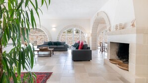 Un amplio espacio habitable con chimenea, paredes de piedra y vistas a través de ventanas arqueadas.