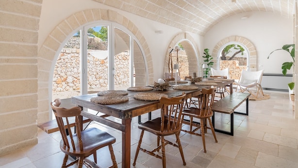 Un comedor con una larga mesa de madera, varias sillas y un fondo de pared de piedra.
