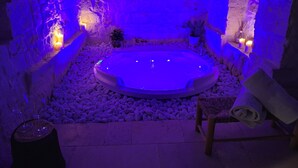 Zona de spa con un jacuzzi rodeado de rocas, velas y una pared de piedra.