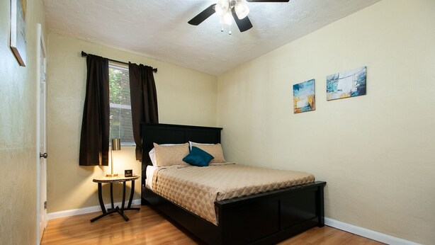 A bedroom with a bed, a bedside table, a lamp, and a ceiling fan. - Charming Farmhouse Relax w/ Heated Massage Chair (Gainesville)
