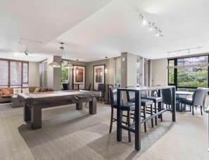 A modern living room with a pool table, dining area, and large windows.