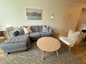 A modern living room with a grey sectional sofa, a round coffee table, and a wicker chair. - Perfectly Located Quality Downtown Home (Victoria)