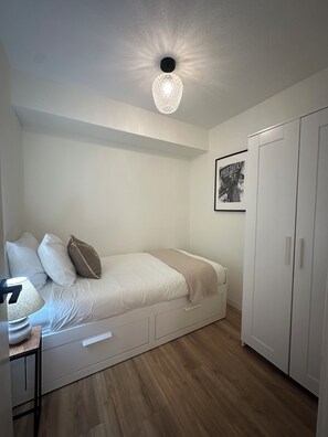 A bedroom with a bed, a bedside table with a lamp, a wardrobe, and a poster on the wall.