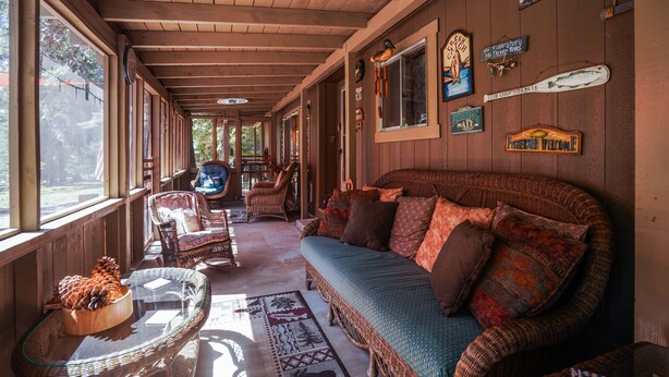 A covered porch with wicker furniture, a glass-top table with pinecones, and various wall decorations. - Upgraded Rustic Themed Retreat w/screened porch in Rocky Point. (Klamath Falls)