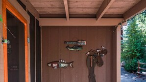 A wooden bench under a covered porch with a wooden door and a sign that reads "Welcome to Our Cabin." - Upgraded Rustic Themed Retreat w/screened porch in Rocky Point. (Klamath Falls)