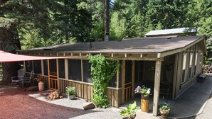 A wooden building with large windows, a covered patio area, and potted plants. - Upgraded Rustic Themed Retreat w/screened porch in Rocky Point. (Klamath Falls)