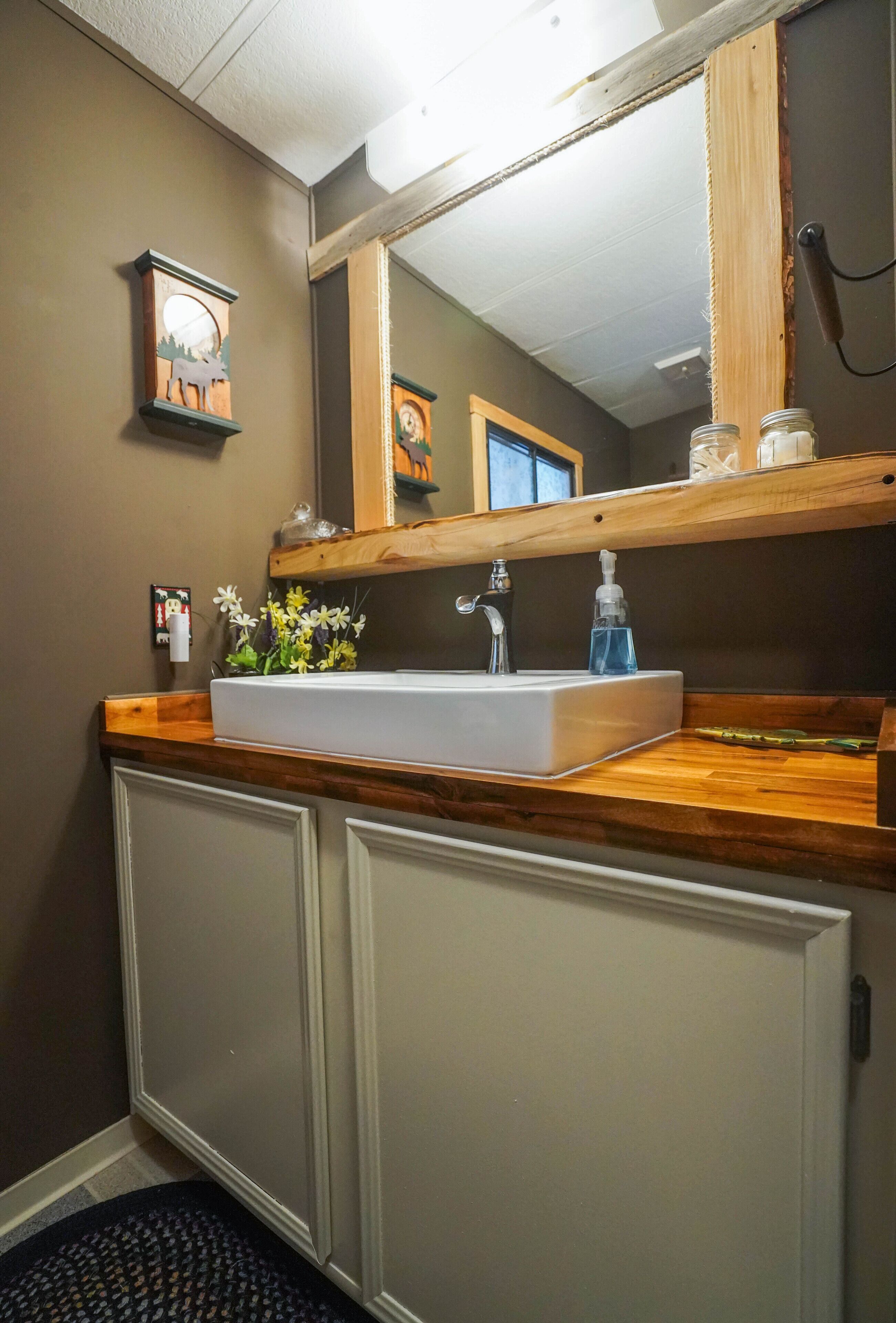 Une salle de bain avec un lavabo blanc, un plan de toilette en bois et un miroir au-dessus.