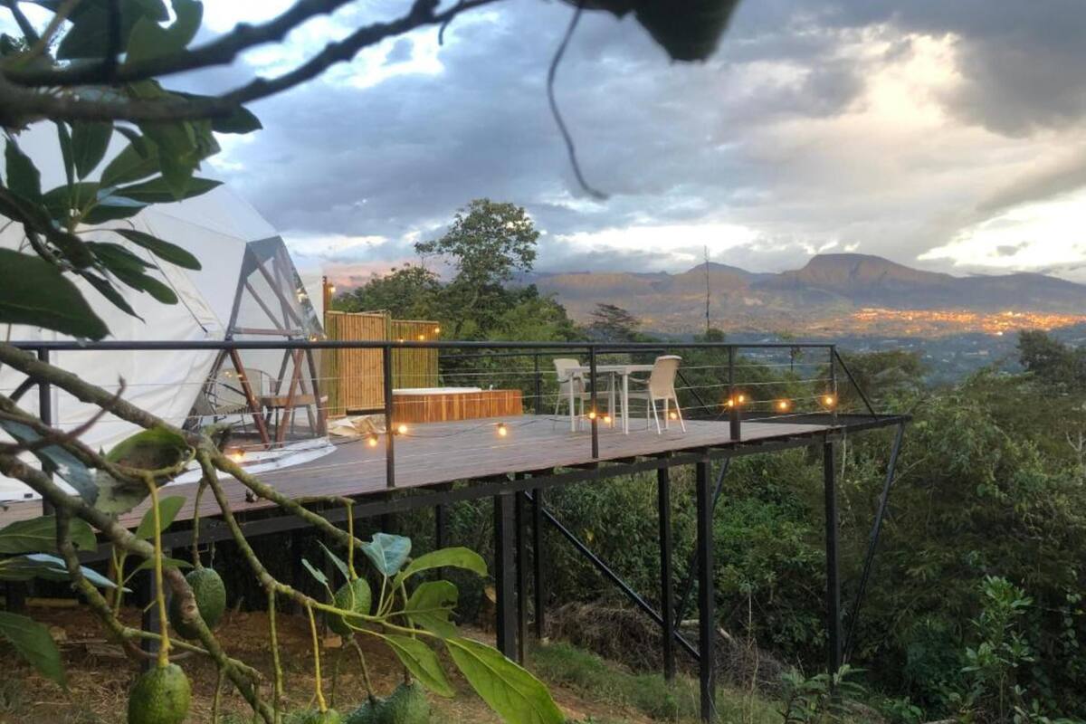 A wooden deck with outdoor seating, overlooking a mountainous landscape and a cityscape in the distance.