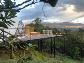 A wooden deck with outdoor seating, overlooking a mountainous landscape and a cityscape in the distance.