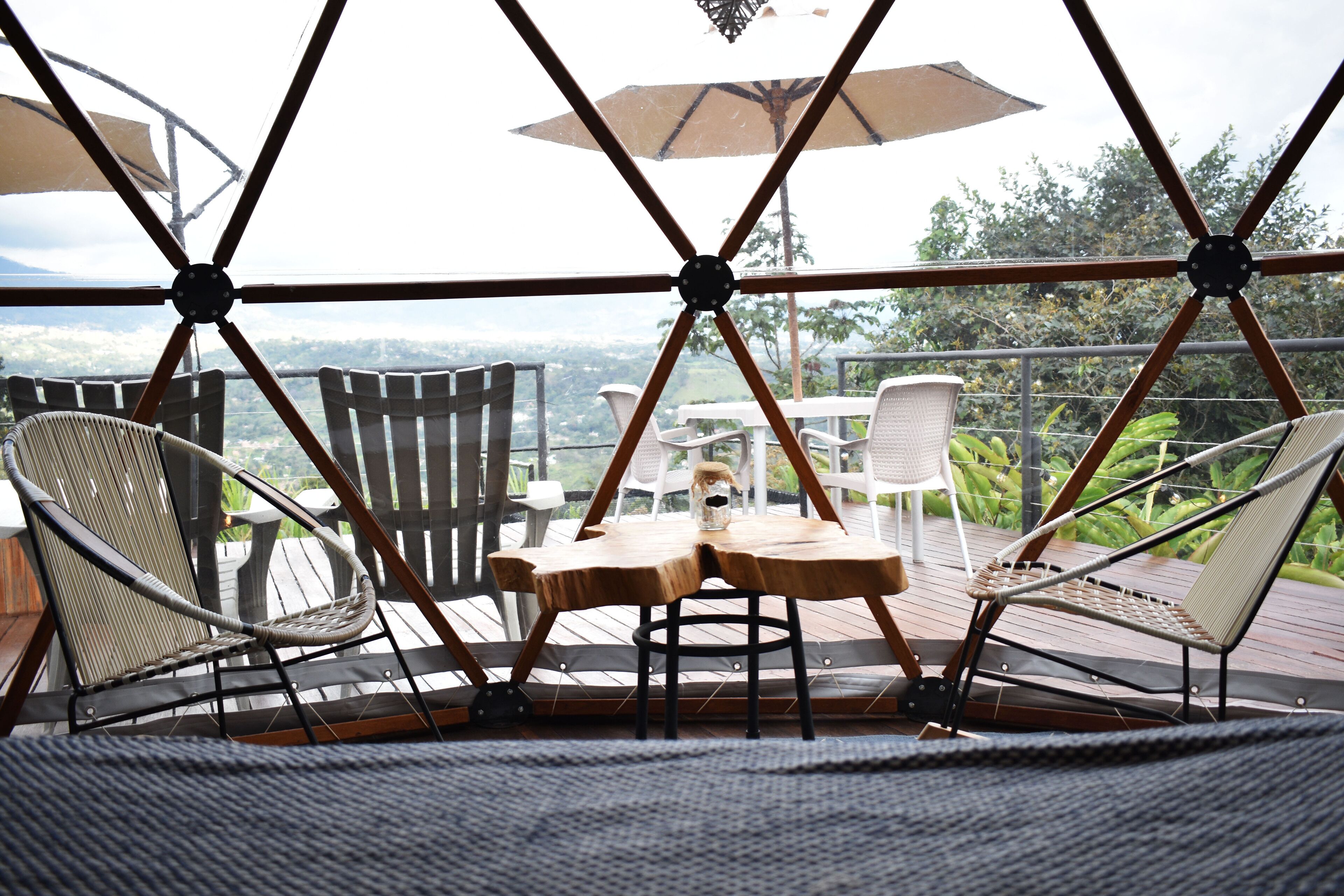 A covered outdoor seating area with chairs and tables, a view of the landscape, and a wooden deck.