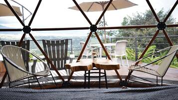 A covered outdoor seating area with chairs and tables, a view of the landscape, and a wooden deck.