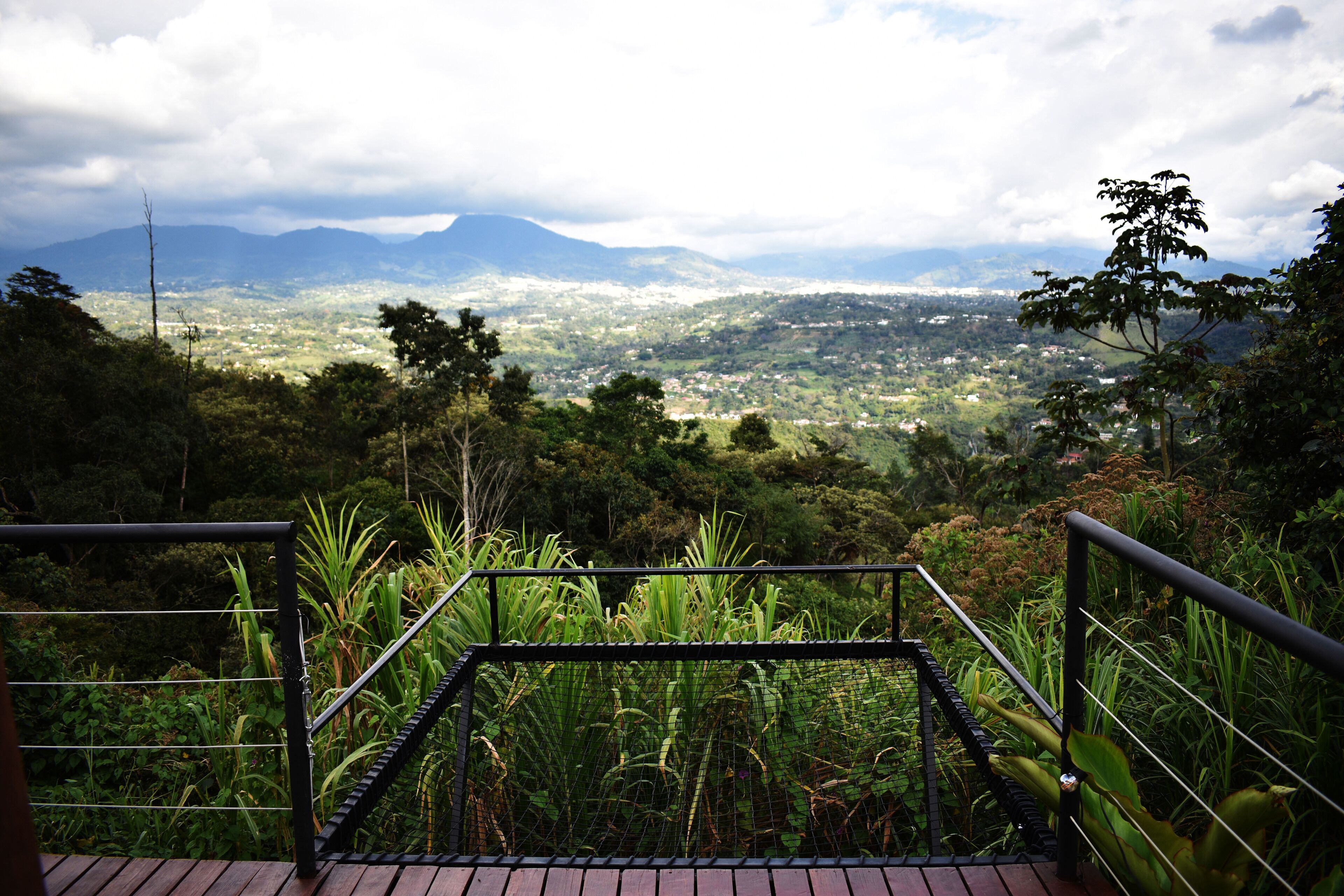 Una escalera conduce a un mirador con vistas a una ciudad lejana y montañas.