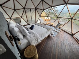 A spacious, high-ceilinged tent-style room with a large bed, wooden flooring, and a view of the surrounding landscape.