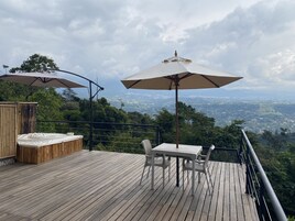 Una terraza de madera con mobiliario exterior y sombrillas, con vistas a un paisaje pintoresco.