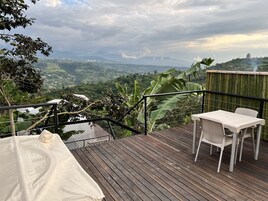 Una terraza de madera con una mesa y sillas, con vistas a un valle exuberante y montañas a lo lejos.