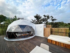 A geodesic dome structure on a wooden deck with a wooden bench and a table.