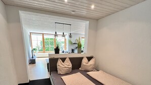 Une chambre moderne avec un grand lit, un petit coin salon et une vue sur la cuisine et le jardin, grâce à de grandes fenêtres.