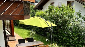 Une terrasse avec une table et des bancs en bois, un parasol jaune et un jardin agrémenté de diverses plantes et fleurs.