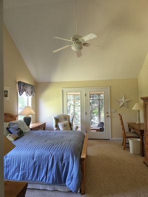 A bedroom with a bed, a chair, a desk, a lamp, a ceiling fan, and a door leading outside.