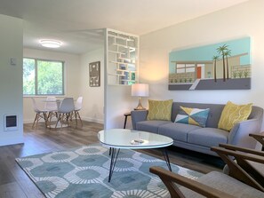 A modern living room with a grey sofa, patterned rug, and a glass coffee table. - Mid Mod Home - 13 Min to Autzen - 6 Min to Airport (Eugene)