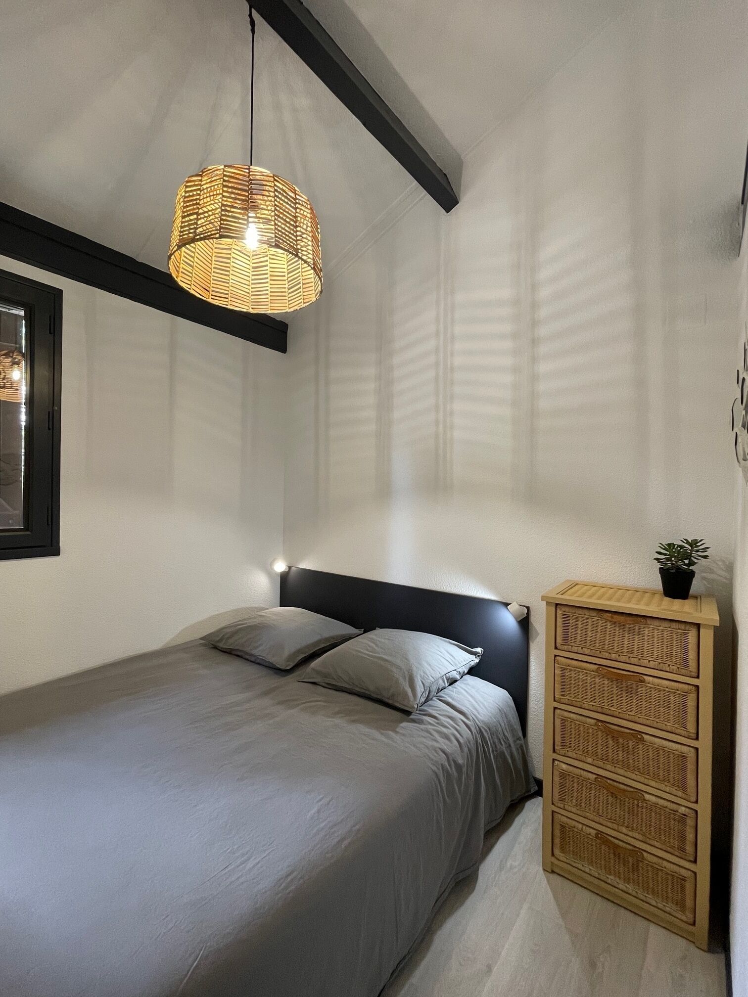 Een slaapkamer met een bed, een nachtkastje met een plant en een hanglamp.