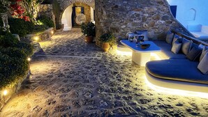 A stone courtyard with a seating area, a stone wall, and a staircase leading to an upper level. - Apanema Villas, Mykonos (Tourlos)