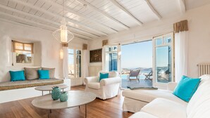 A spacious living room with a high ceiling, white sofas, a round coffee table, and a view of the sea through large windows. - Apanema Villas, Mykonos (Tourlos)