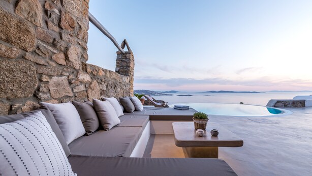 A modern outdoor seating area with a stone wall, a sofa, and a small table with a plant and a pot. - Apanema Villas, Mykonos (Tourlos)