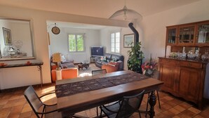 Een eethoek met een lange houten tafel, zwarte stoelen en een tafelkleed met een patroon. Er is een houten kast met glazen deuren en een spiegel aan de muur.