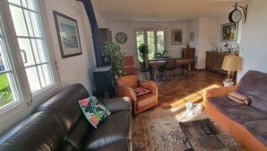 Een gezellige woonkamer met een leren bank, een bruine fauteuil en een kamerbreed tapijt. In de achtergrond is een eethoek met een tafel en stoelen te zien.