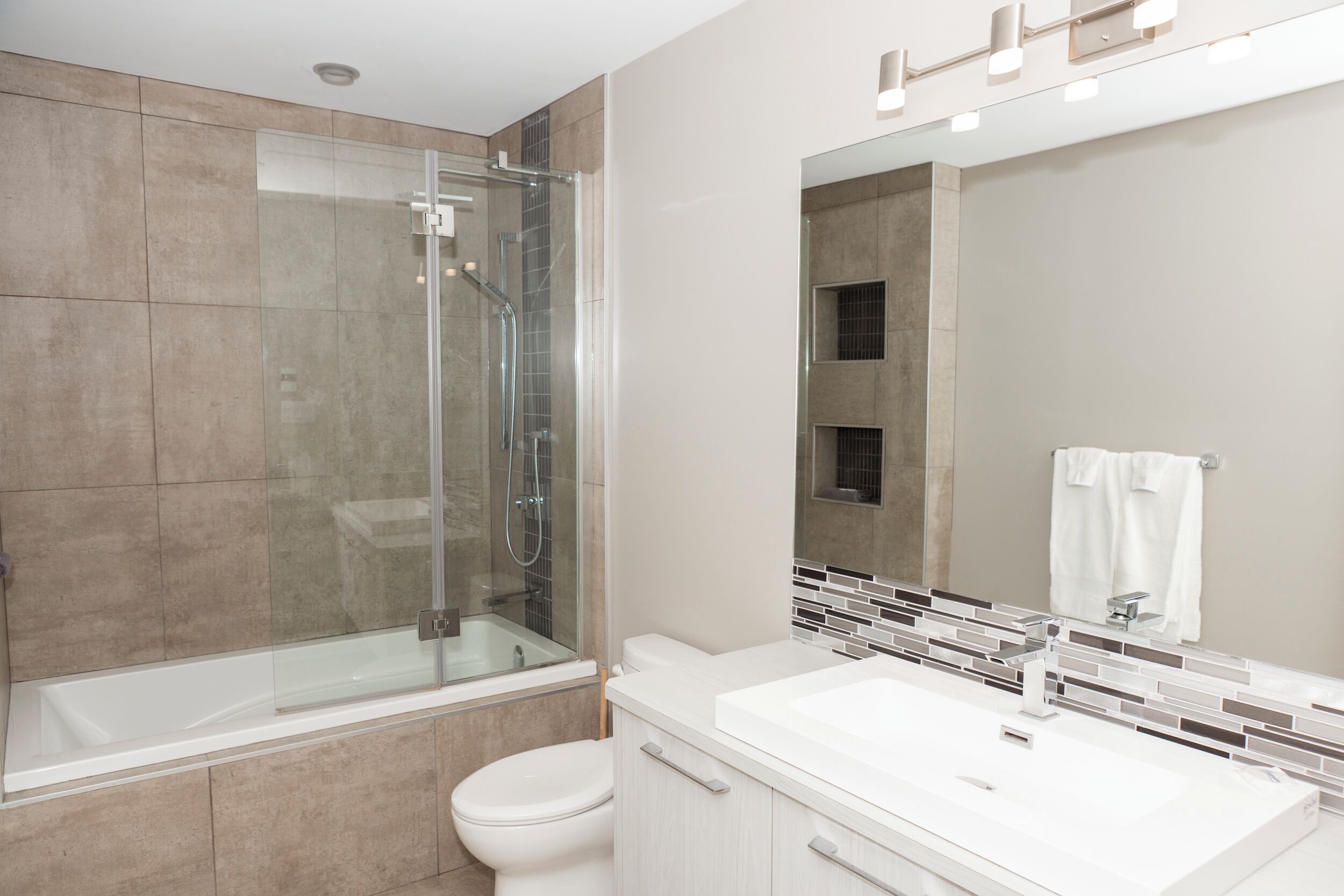 A modern bathroom with a glass-enclosed shower, a white toilet, and a vanity with a mirror.