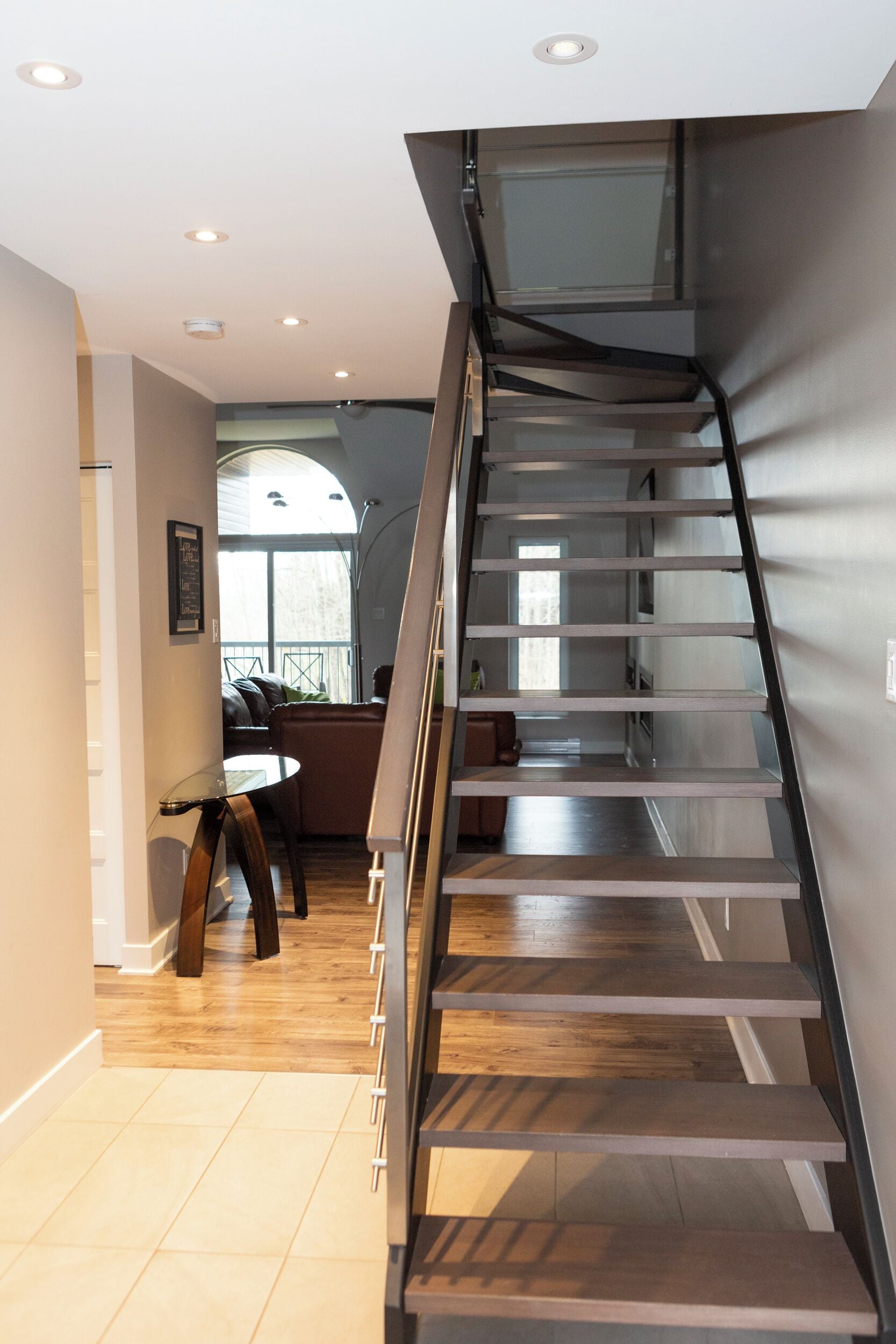 A modern interior with a staircase leading to an upper level, a dining area with a table and chairs, and a view of the outdoors.