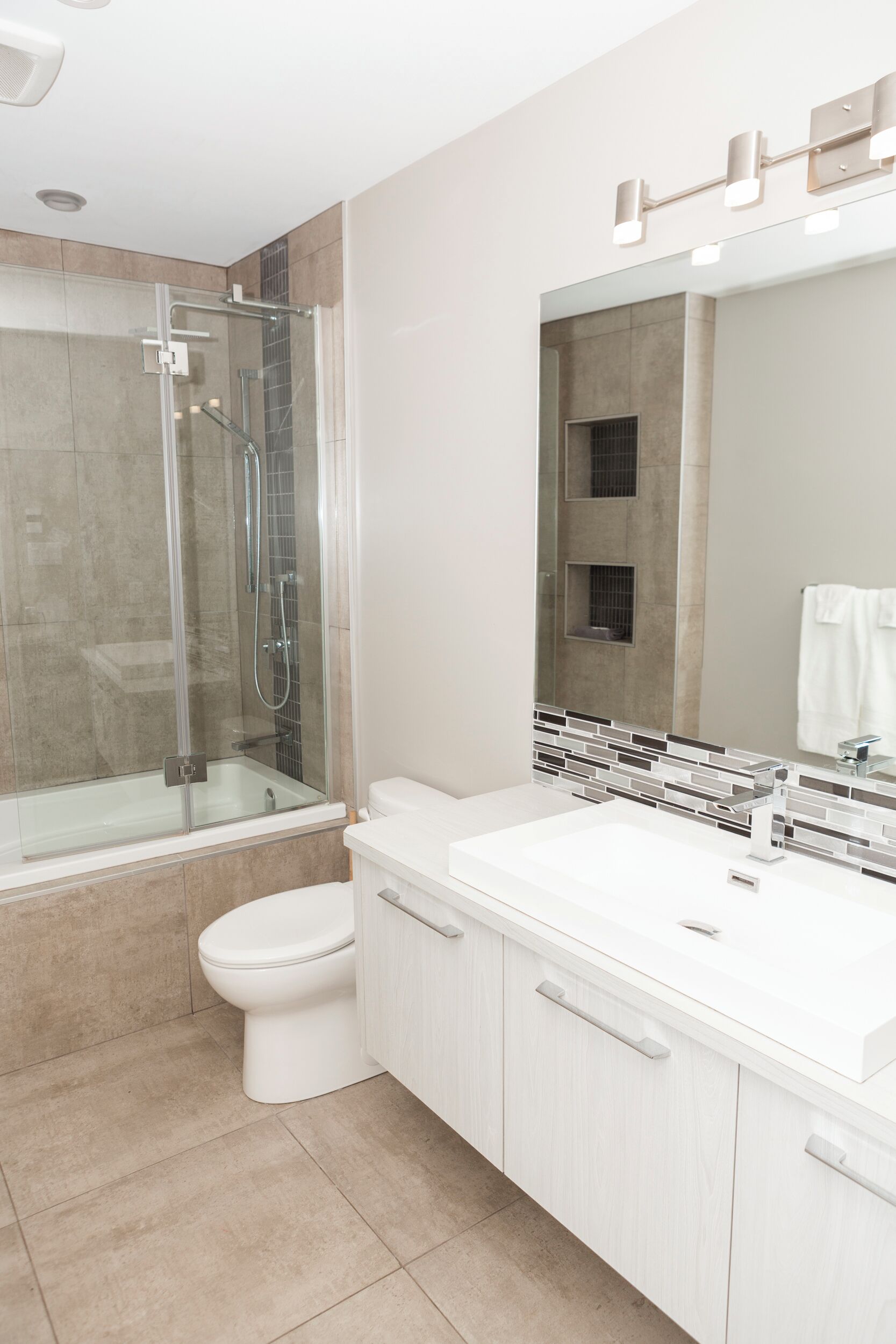 A modern bathroom with a glass-enclosed shower, a white toilet, and a large vanity with a mirror.