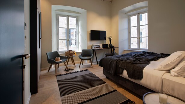 Un dormitorio moderno con una cama, dos sillones, un escritorio y un televisor.